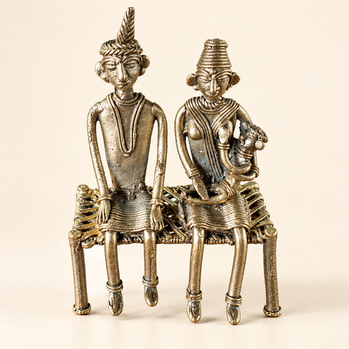 An antique-style metal figurine depicting a seated couple on a woven chair, crafted in a textured metallic finish with warm bronze and silver tones, set against a plain beige background.