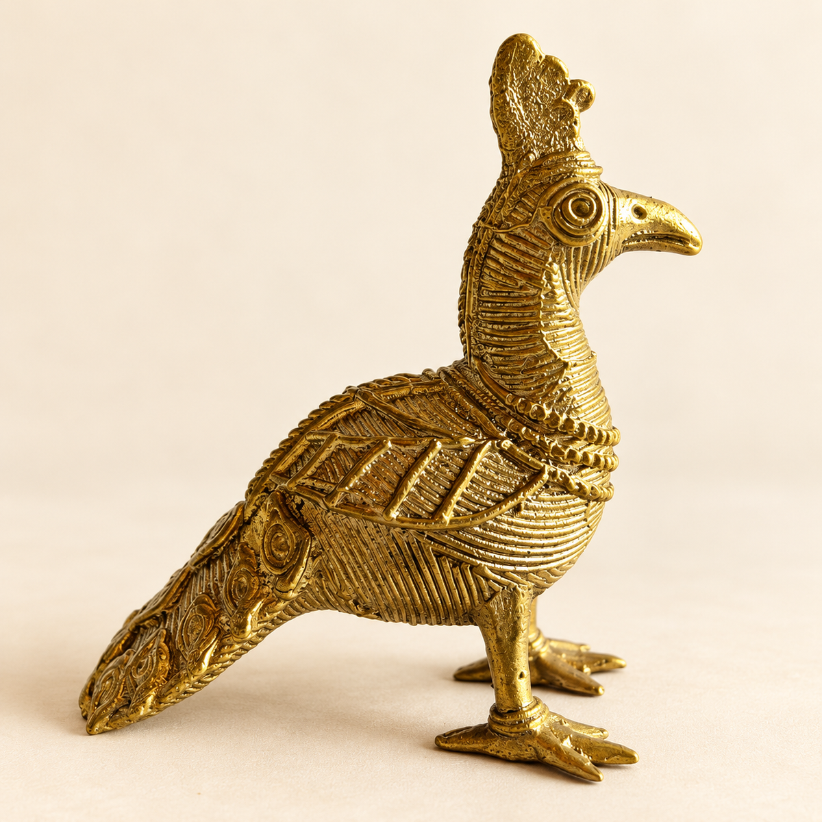 Dokra-inspired golden peacock figurine with intricate feather patterns and traditional detailing, displayed against a warm cream background by Kalavan.